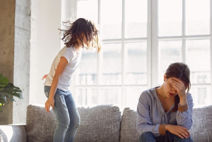 kid jumping on the sofa and the mom is tired