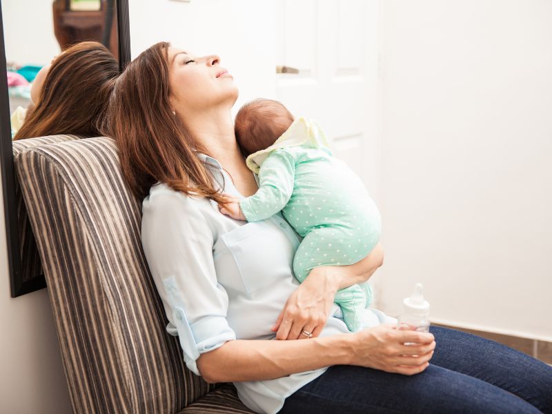 a tired new mom sleeping on a chair with a newborn in her hand