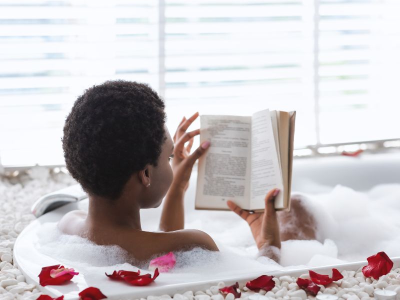 a woman sitting on a bathtub with a book - mom self care