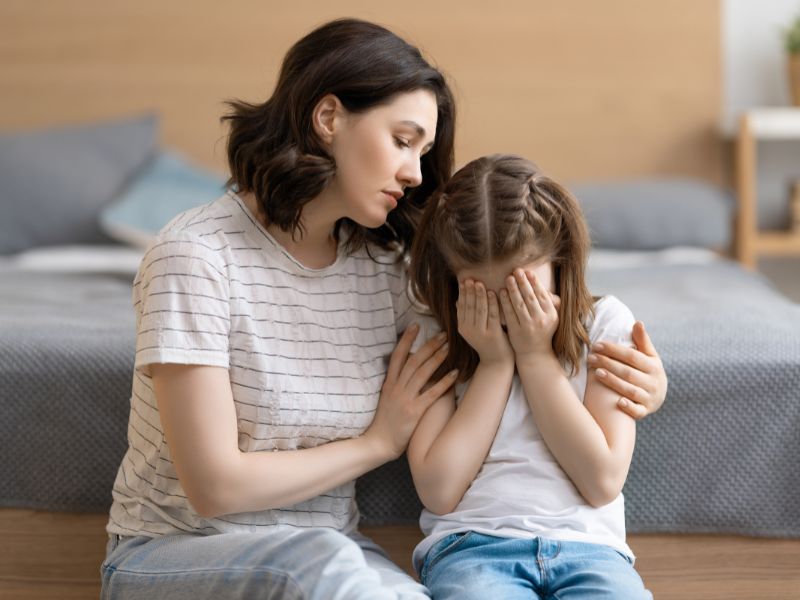 a crying girl is consoled by her mom