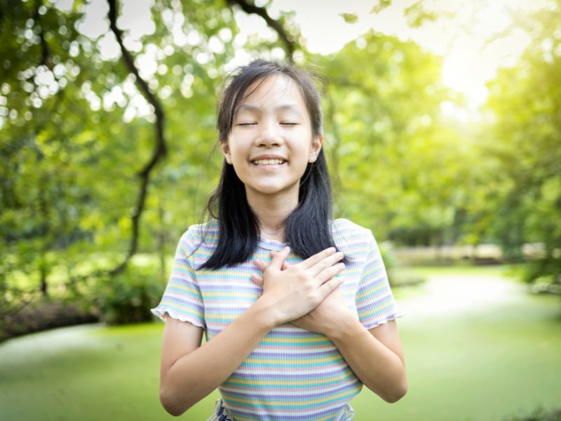 a girl placing hands on her heart, eyes closed and smiling-nature play for kids