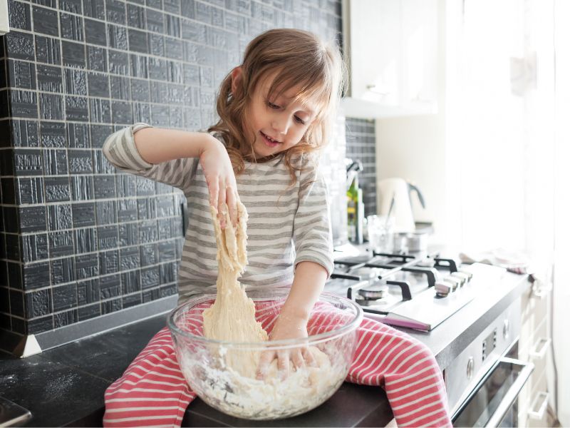 a small girl kneading the dough