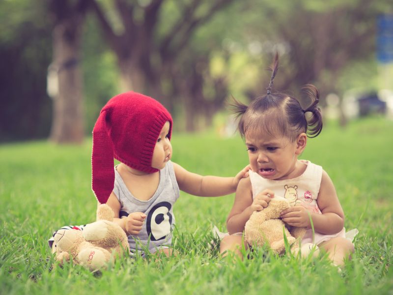 two babies sitting, one is crying and the other is consoling her-nature play for kids