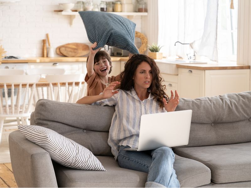 a mom is frustrated by her child while working on a laptop